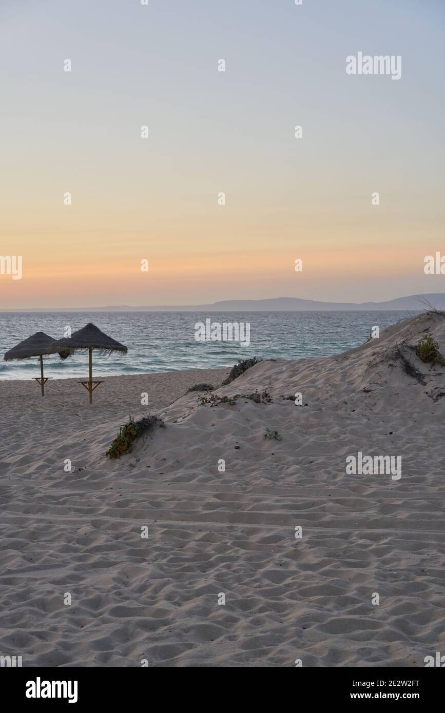 Leerer Strand bei Sonnenuntergang in Comporta, Portugal mit Strohsonnenschirmen Stockfoto