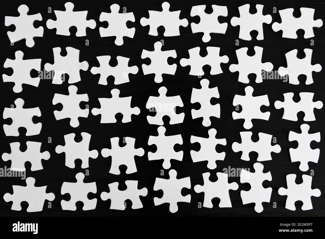 Gitter Reihen von weißen Puzzle-Stücke auf einem schwarzen Tabelle Stockfoto