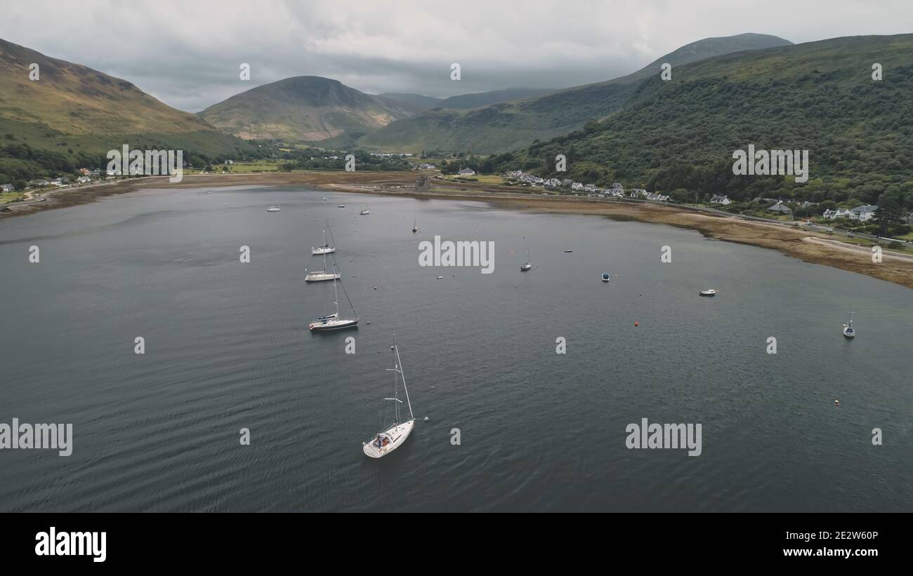 Yachten, Boote, Schiffe in Schottland Meeresbucht Antenne. Epische Berglandschaft am bewölkten Sommertag von Drohne erschossen. Filmischer Meeresurlaub an grünen Bergen an der Küste. Loch Ranza Bay, Arran Island. Stockfoto