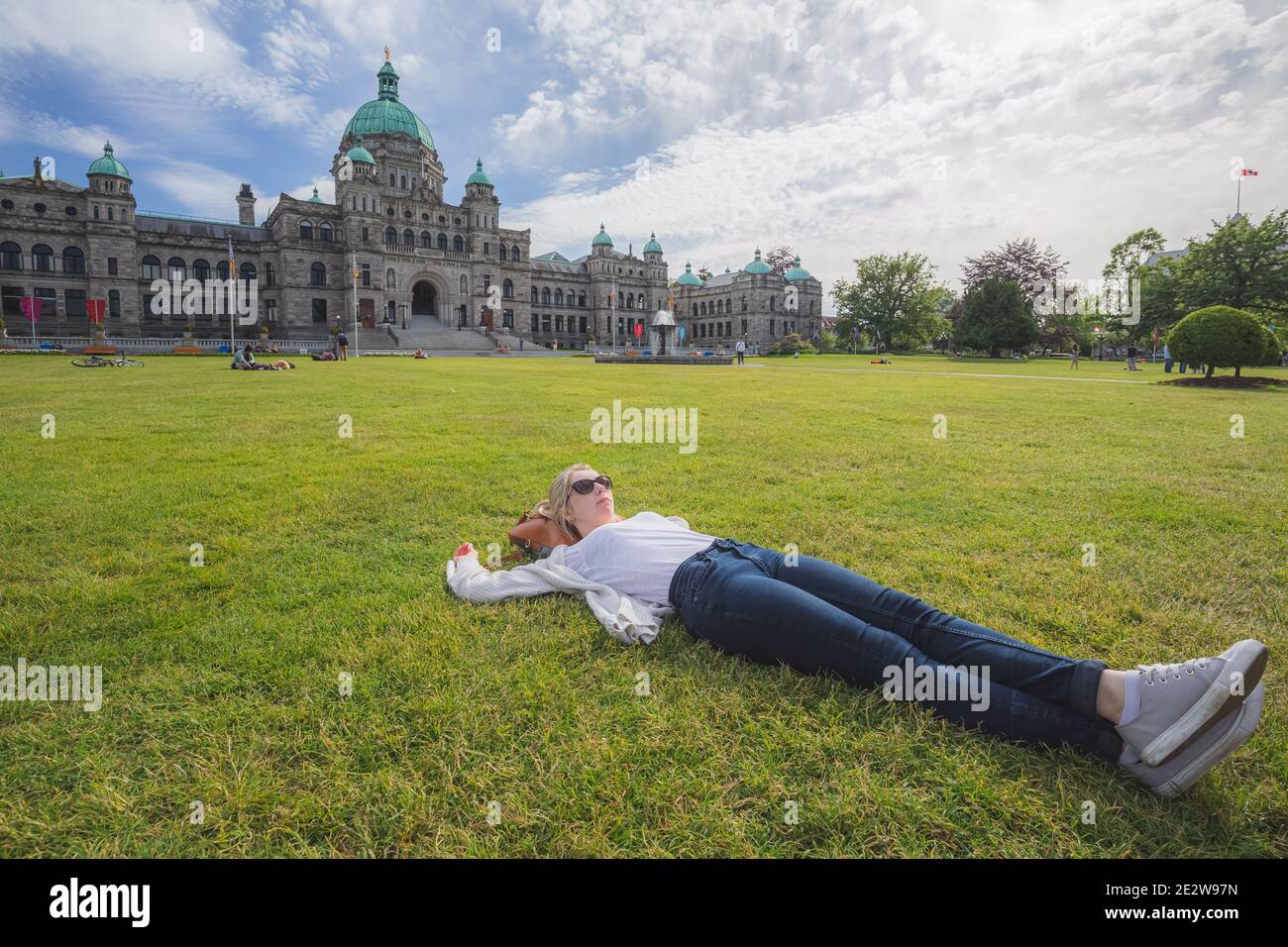 Eine junge Frau entspannt sich auf dem Rasen vor der Legislative Assembly of British Columbia an einem sonnigen Tag in Victoria, Kanada. Stockfoto