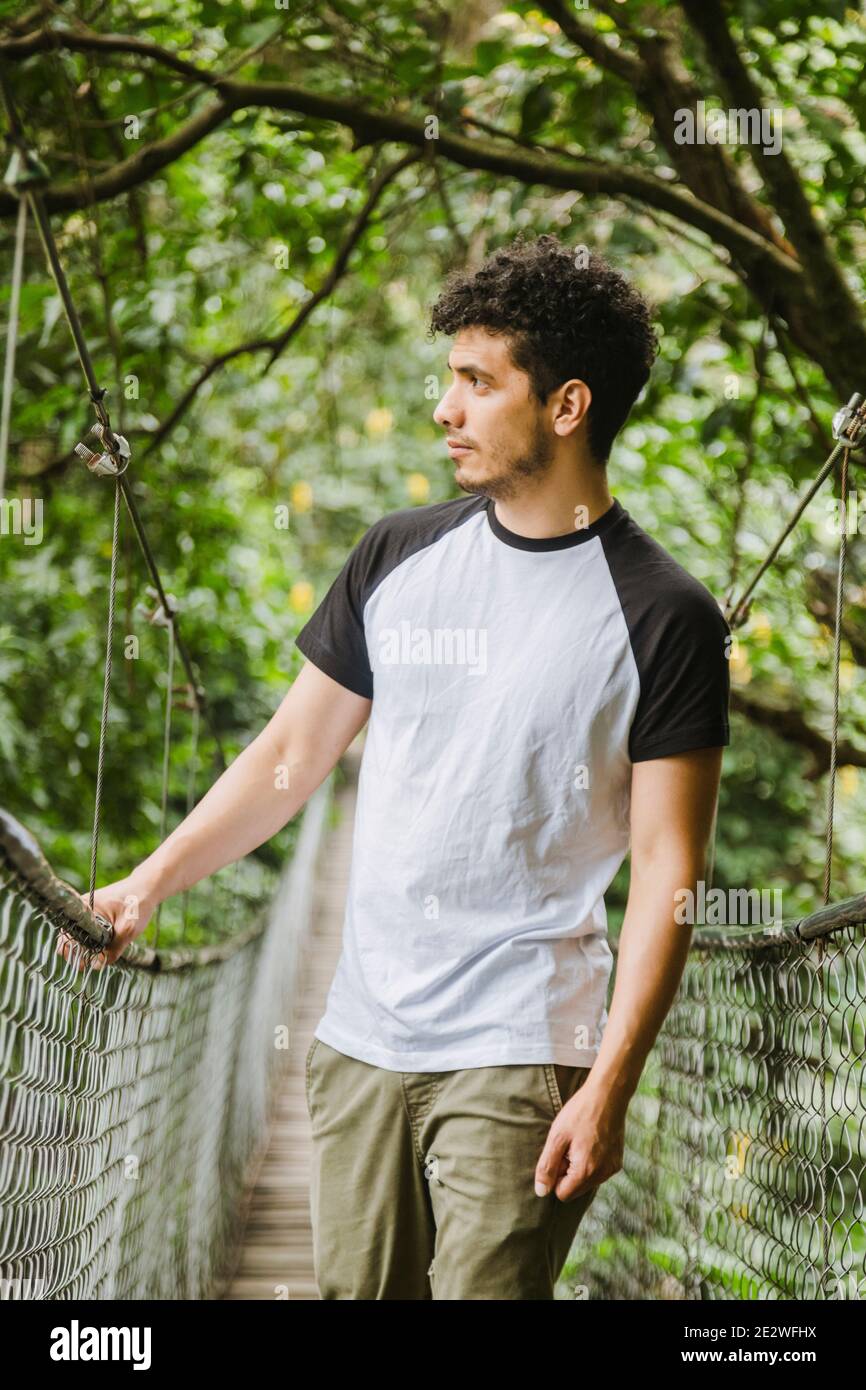 Junger hispanischer Mann, der auf einer Hängebrücke in der geht Mitten im Wald - junger Reisender, der beim Beobachten spazierengeht Natur und genießen Sie die Fahrt - Stockfoto