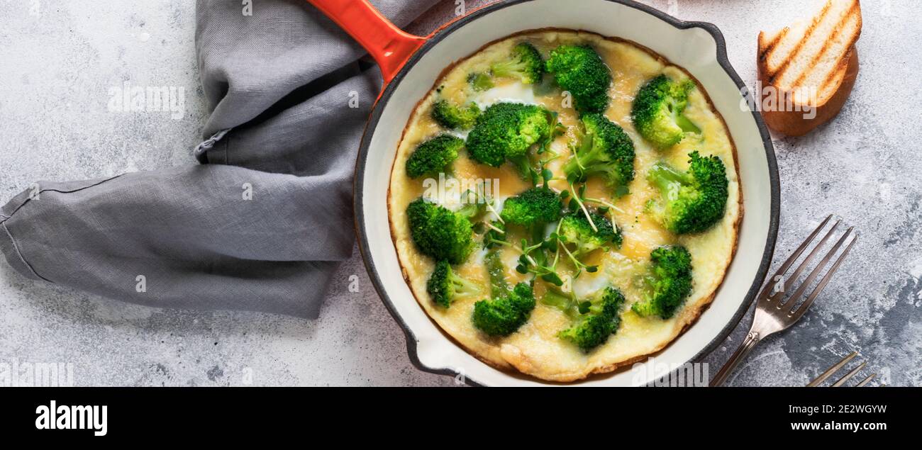 Omelette mit Brokkoli und grünen jungen Zwiebeln auf rotem Gusseisen Pfanne auf alten grauen Beton Hintergrund. Draufsicht. Stockfoto