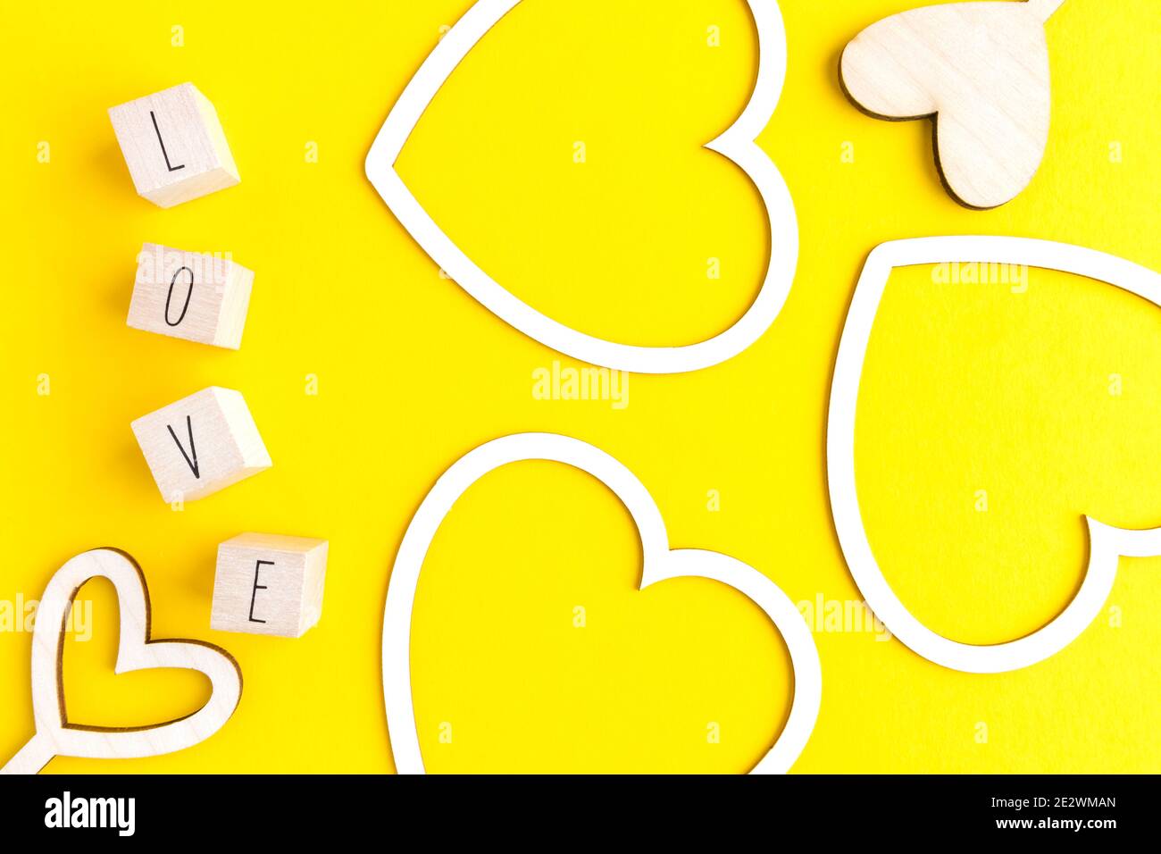 Flache Herzformen aus weißem Karton, Holz und Buchstaben mit dem Wort Liebe auf gelbem Hintergrund mit Platz für Text. Stockfoto