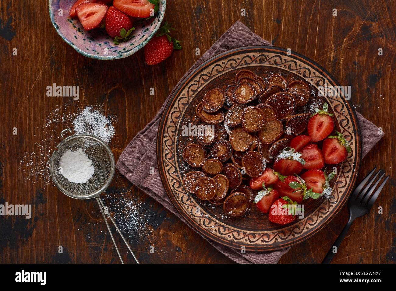 Mini-Schokolade Pfannkuchen Müsli mit Erdbeeren zum Frühstück auf alten Holztisch. Trendiges Frühstück mit winzigen Pfannkuchen. Stockfoto