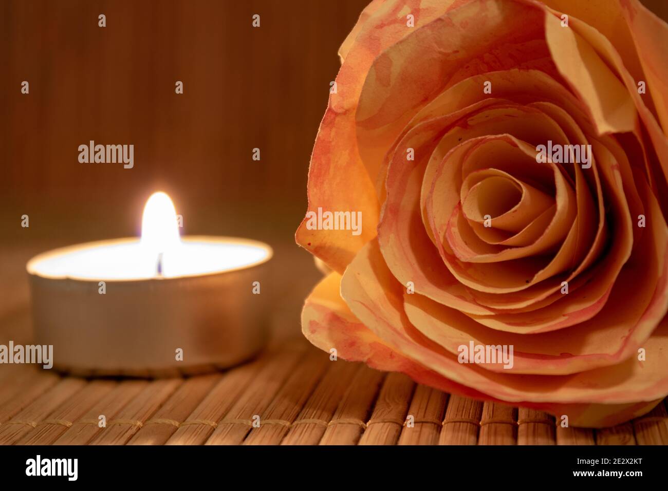 Rosenblüte und brennende Kerze. Rosenblüte aus Papier mit Teelicht auf Holztisch mit Kopierfläche liegend. Romantisches Konzept Stockfoto