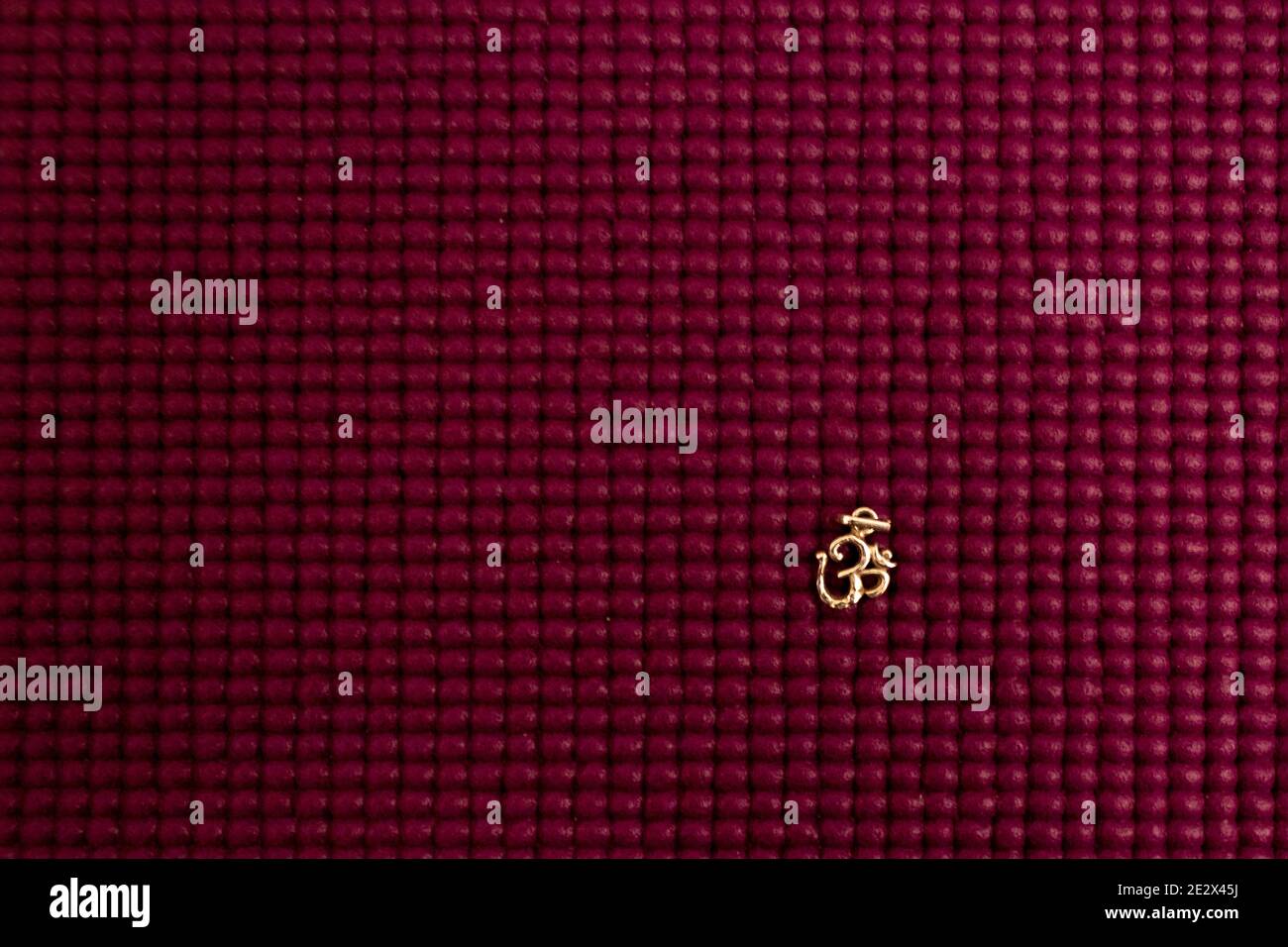 Minimalistische Nahaufnahme eines goldenen OM-Symbols auf einem strukturierten Burgunderhintergrund Stockfoto