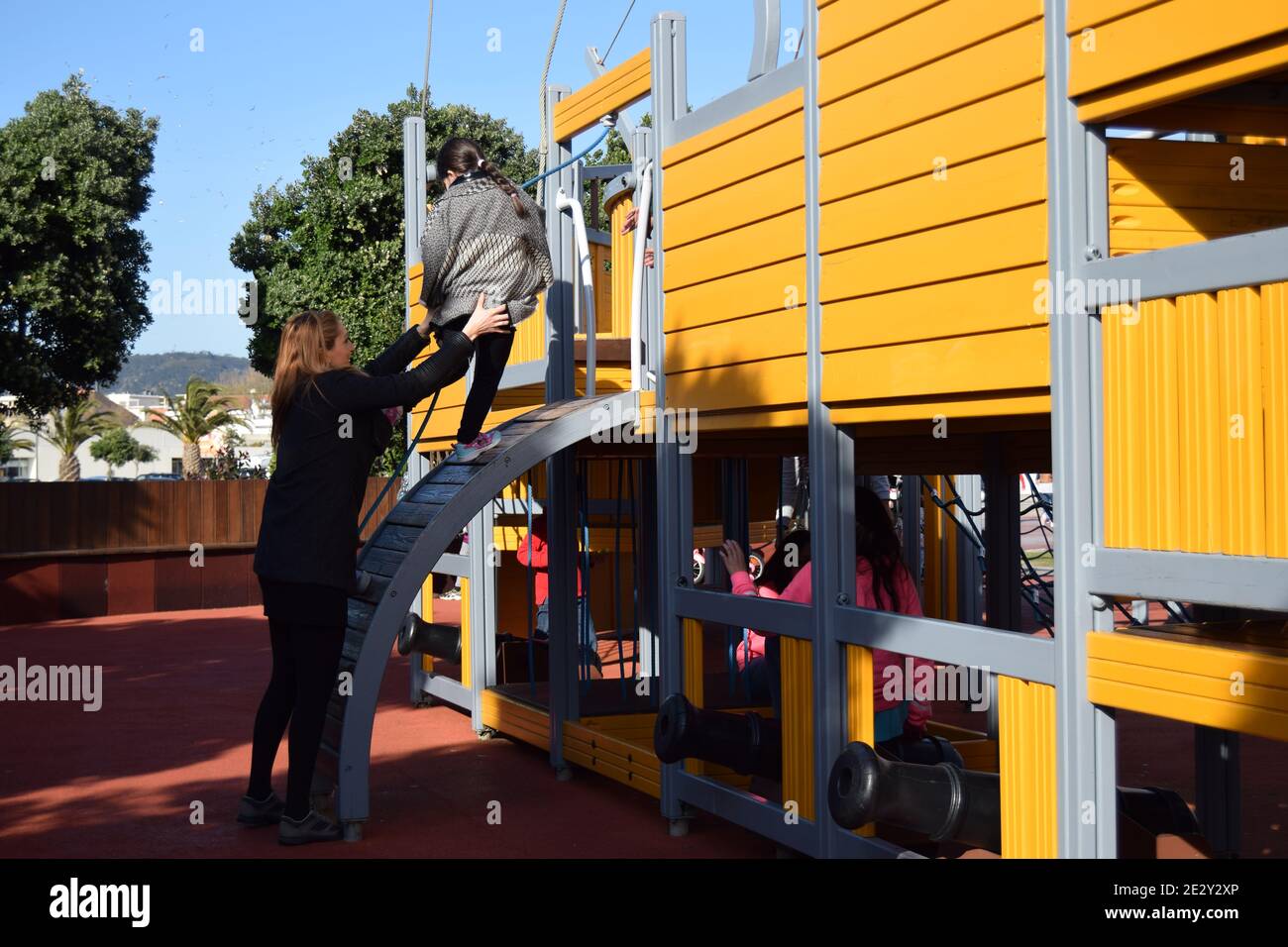 Alleinerziehende Mutter hilft seiner Tochter, auf dem Spielplatz Attraktion zu klettern Stockfoto