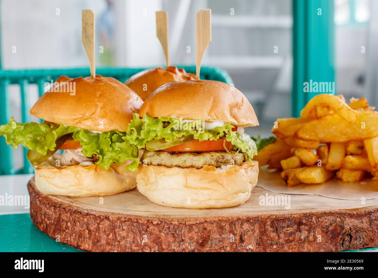 Drei Fischschuppen (Mini-Burger) mit Salat, Tomaten und Gurken, serviert mit pommes frites auf einem Holztablett Stockfoto