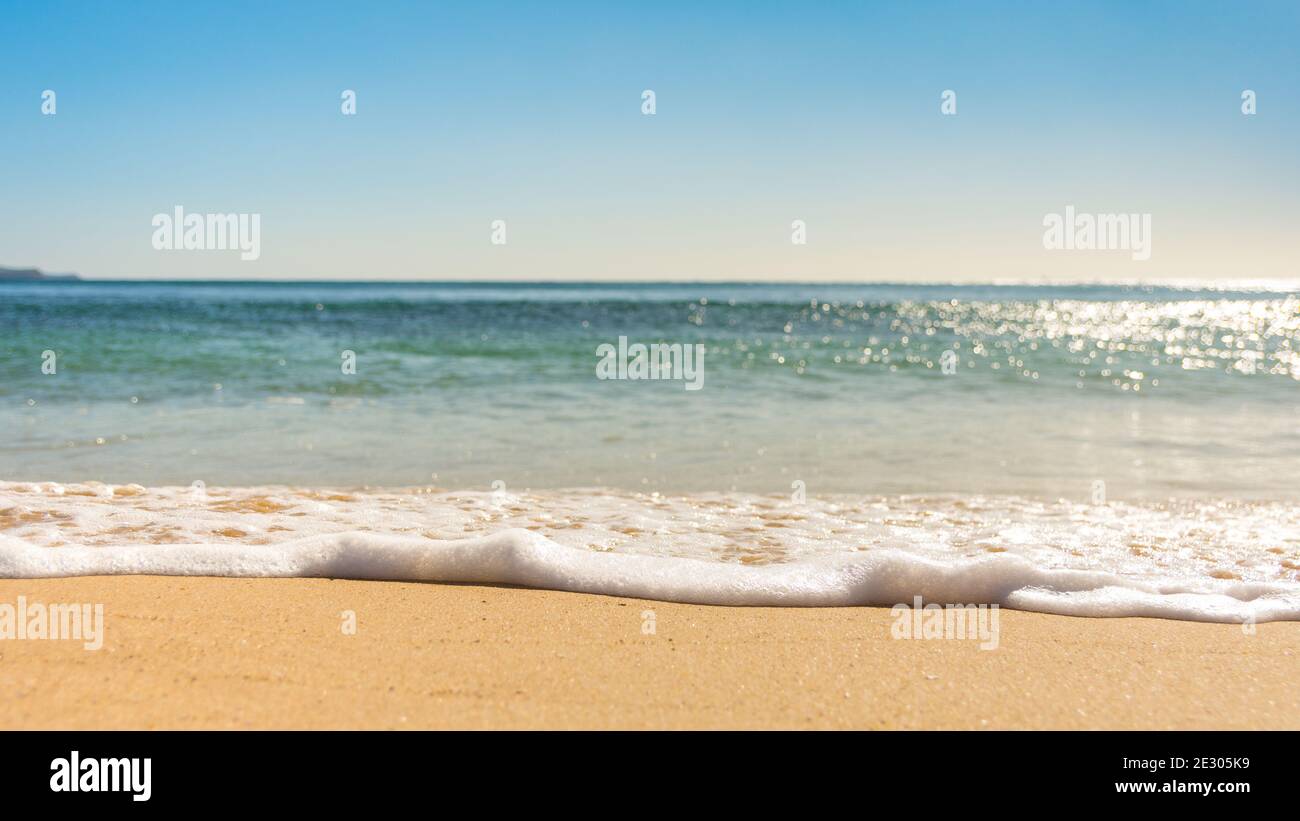 Wellen Sie sich an schönen sonnigen Tagen über den Sand Stockfoto