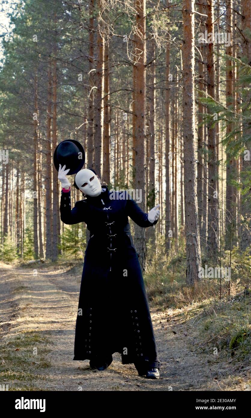 Eine maskierte Frau mit schwarzem Hut im Kiefernwald Stockfoto