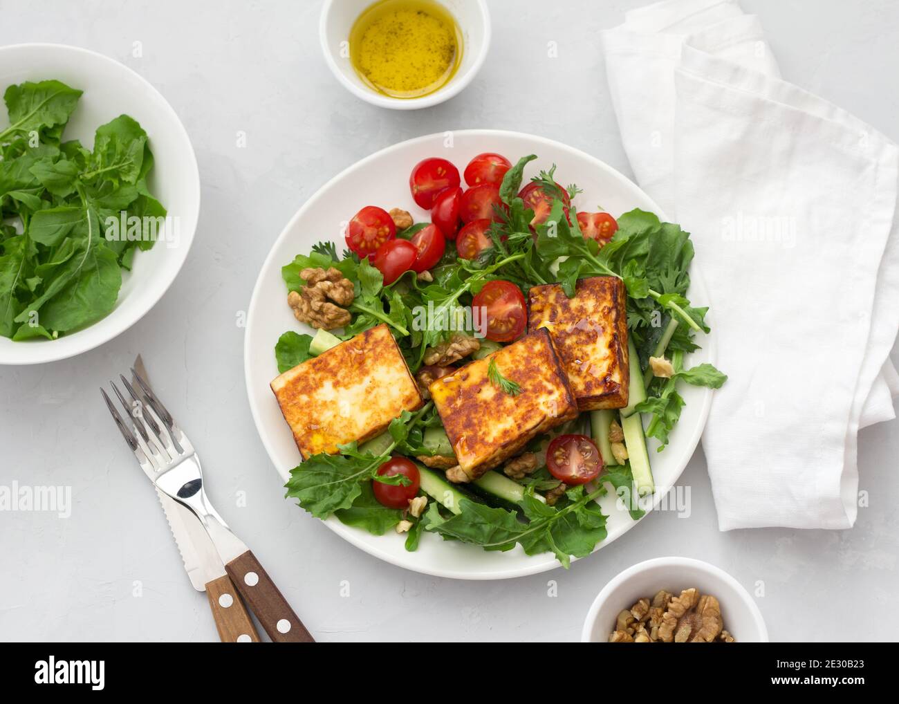 Frischer Salat aus Rucola, Kirschtomaten, Gurken und gebratenem Käse auf grauem Steingrund. Draufsicht. Leckere gesunde Lebensmittel Stockfoto