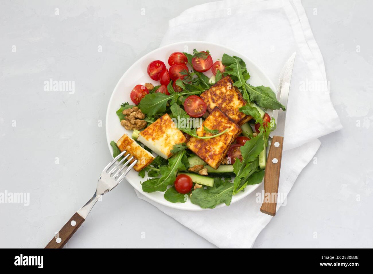 Frischer Salat aus Rucola, Kirschtomaten, Gurken und gebratenem Käse auf grauem Steingrund. Draufsicht. Leckeres gesundes Essen. Freiraum Stockfoto