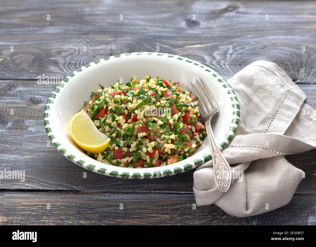 Tabbouleh, traditioneller arabischer Salat aus Bulgur, Petersilie und Tomaten auf einem Holztisch. Köstliche Diät-Essen Stockfoto