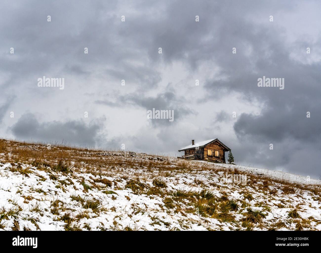 Blockhütte in den Dolomiten mit dem ersten Schnee oktober mit dunklen verschneiten Wolken am Himmel Stockfoto