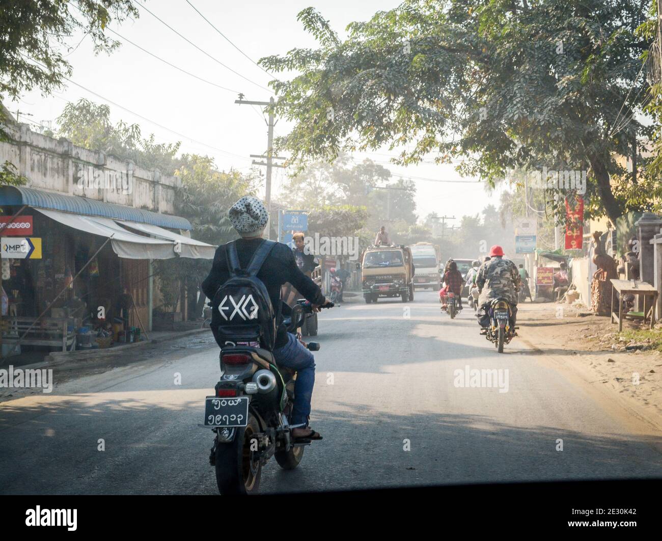 Mandalay, Myanmar - Landstraße voll mit Motorrädern und Lastwagen am Morgen. Ein Mann mit EXO Rucksack. Stockfoto