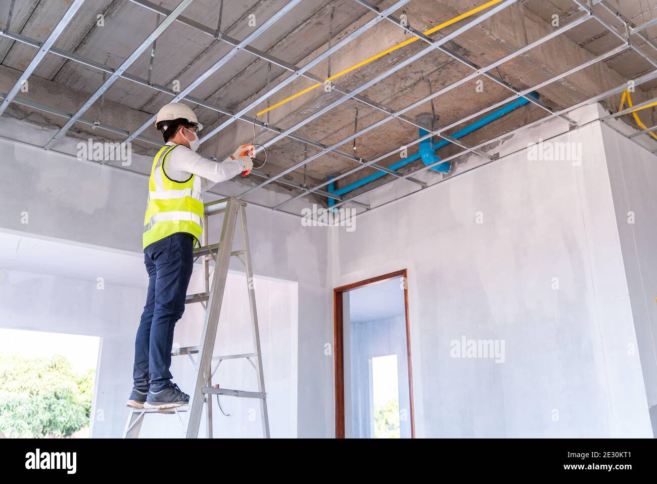 Asiatische Elektriker trägt eine Maske Installation Verlegung Elektrokabel an der Decke mit Zangen im Haus im Bau. Stockfoto