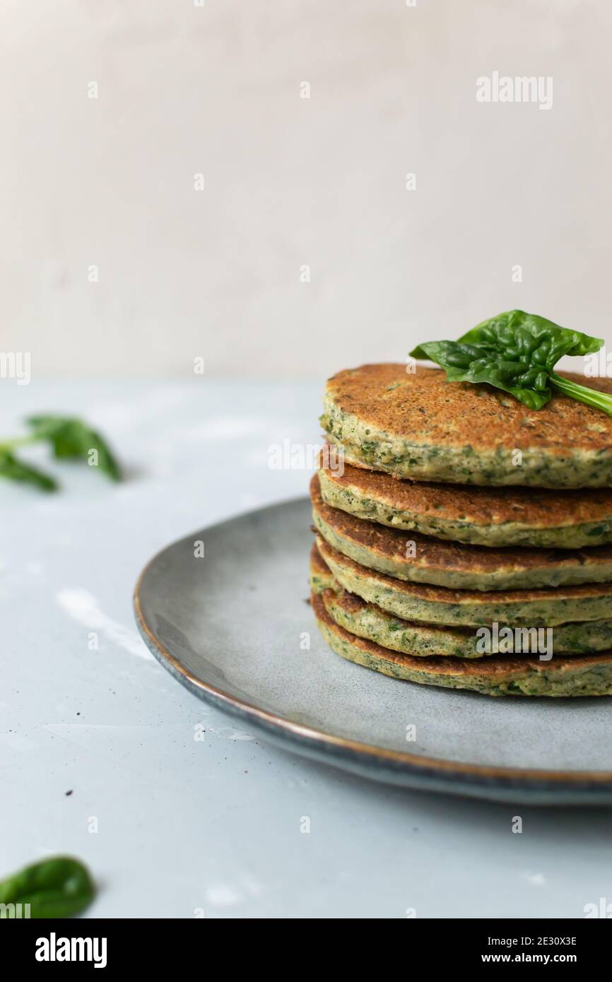 Spinat- und Bananenpfannkuchen und grüne Blätter auf einem grauen Teller auf grauem Hintergrund. Gesunde Ernährung Konzept. Speicherplatz kopieren. Vertikale Ausrichtung. Stockfoto