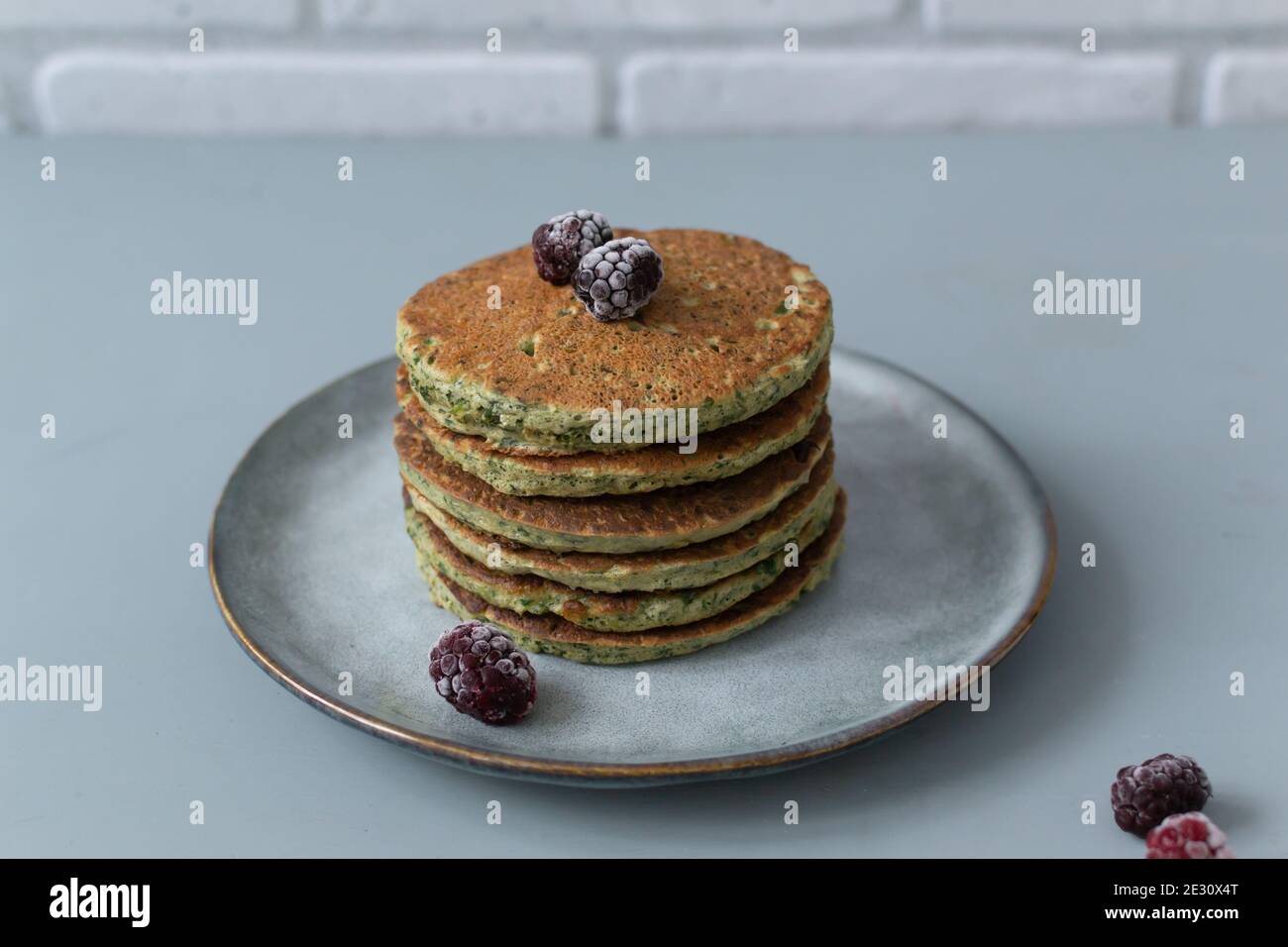 Spinat- und Bananenpfannkuchen mit gefrorenen Beeren auf einem grauen Teller auf grauem Hintergrund. Gesunde Ernährung Konzept. Horizontale Ausrichtung. Speicherplatz kopieren. Stockfoto