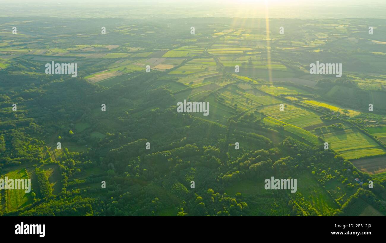 Sonnenschein Bokeh über grünen Dunst hügelige Landschaft, mehrere kultivierte Parzellen zwischen Waldbäumen in frühen Morgenstunden. Stockfoto