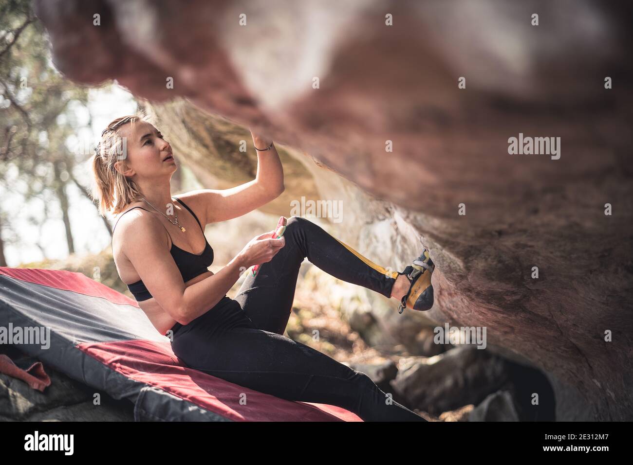 Eine starke Frau bereitet sich darauf vor, einen überhängenden Felsbrocken beim Bouldern in Fontainebleau, Frankreich, zu besteigen Stockfoto