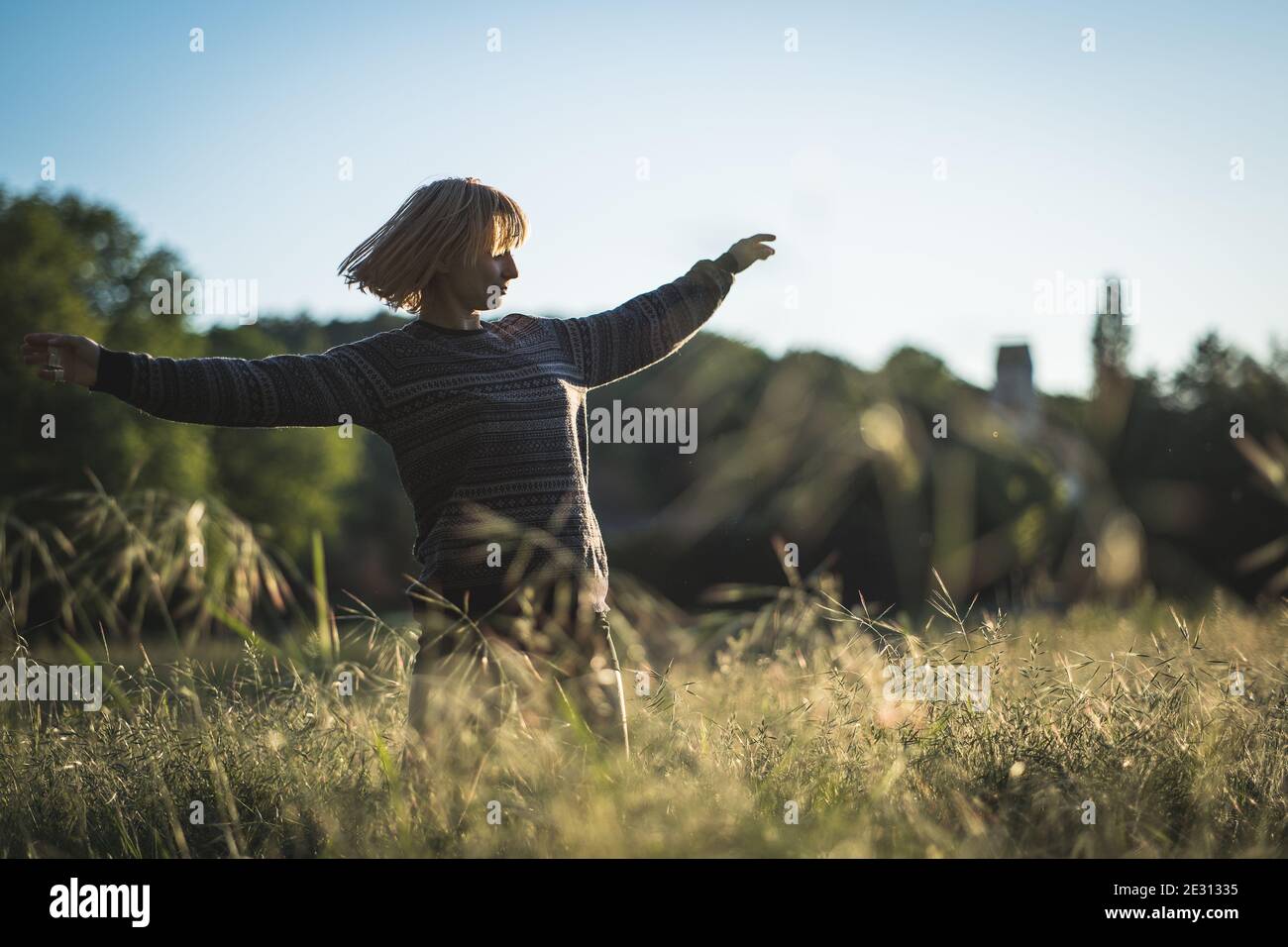 Eine junge Frau, die während der goldenen Stunde im hohen Gras tanzt Stockfoto