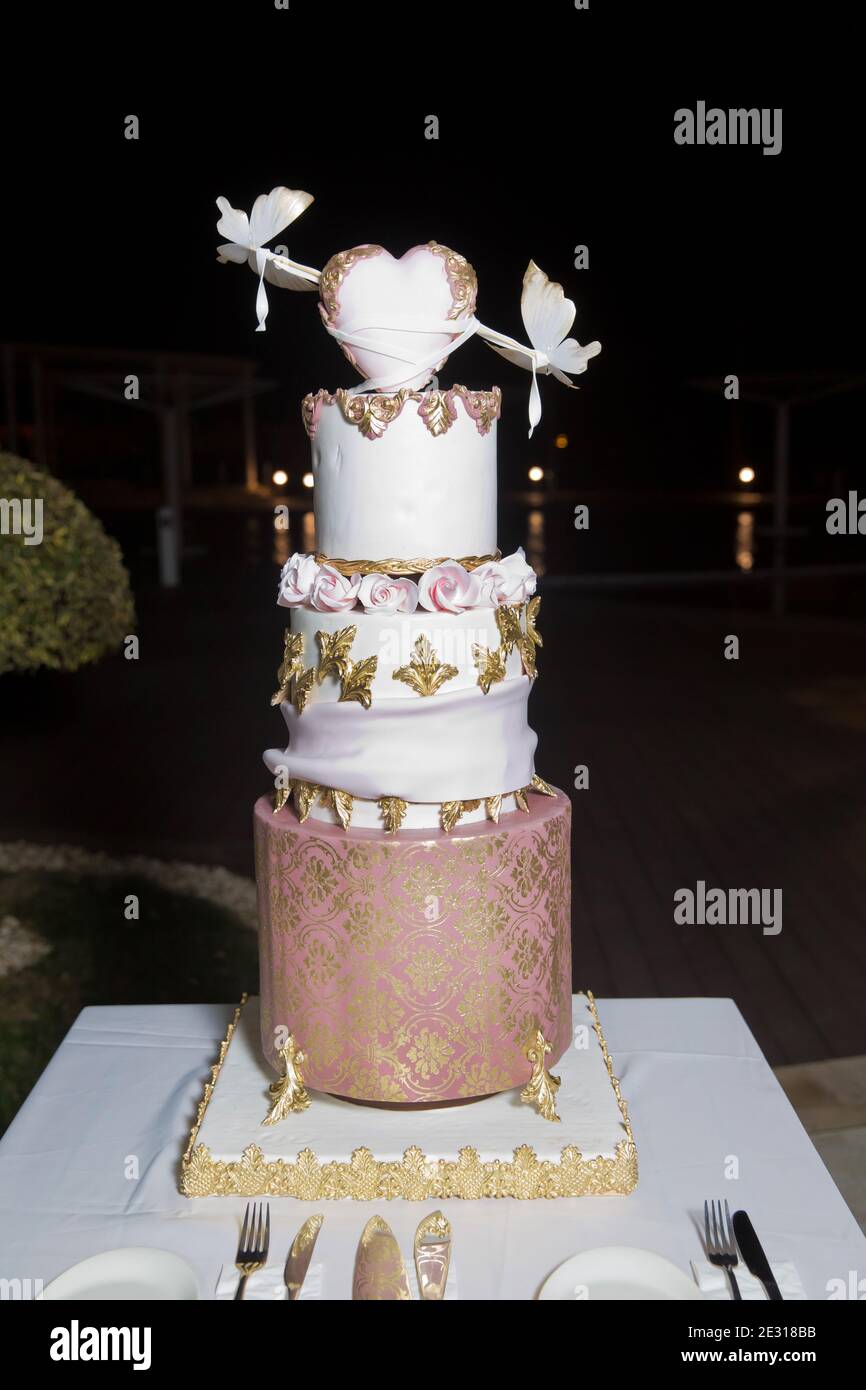 Dreilagiger weißer Kuchen. Weißer Herzkuchen auf dem Kuchen. In Gold dekoriert. Hochzeitstorte in der Halle Stockfoto