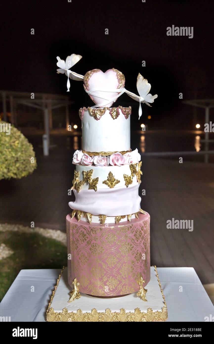 Dreilagiger weißer Kuchen. Weißer Herzkuchen auf dem Kuchen. In Gold dekoriert. Hochzeitstorte in der Halle Stockfoto