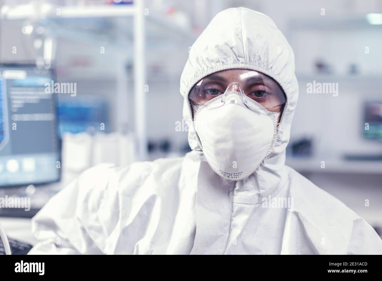 Porträt eines erschöpften Chemikers, der in einem modern ausgestatteten Labor die Kamera mit Overall betrachtet. Müde Frau Wissenschaftlerin in Biotechnologie-Labor trägt Schutzanzug während der globalen Epidemie. Stockfoto