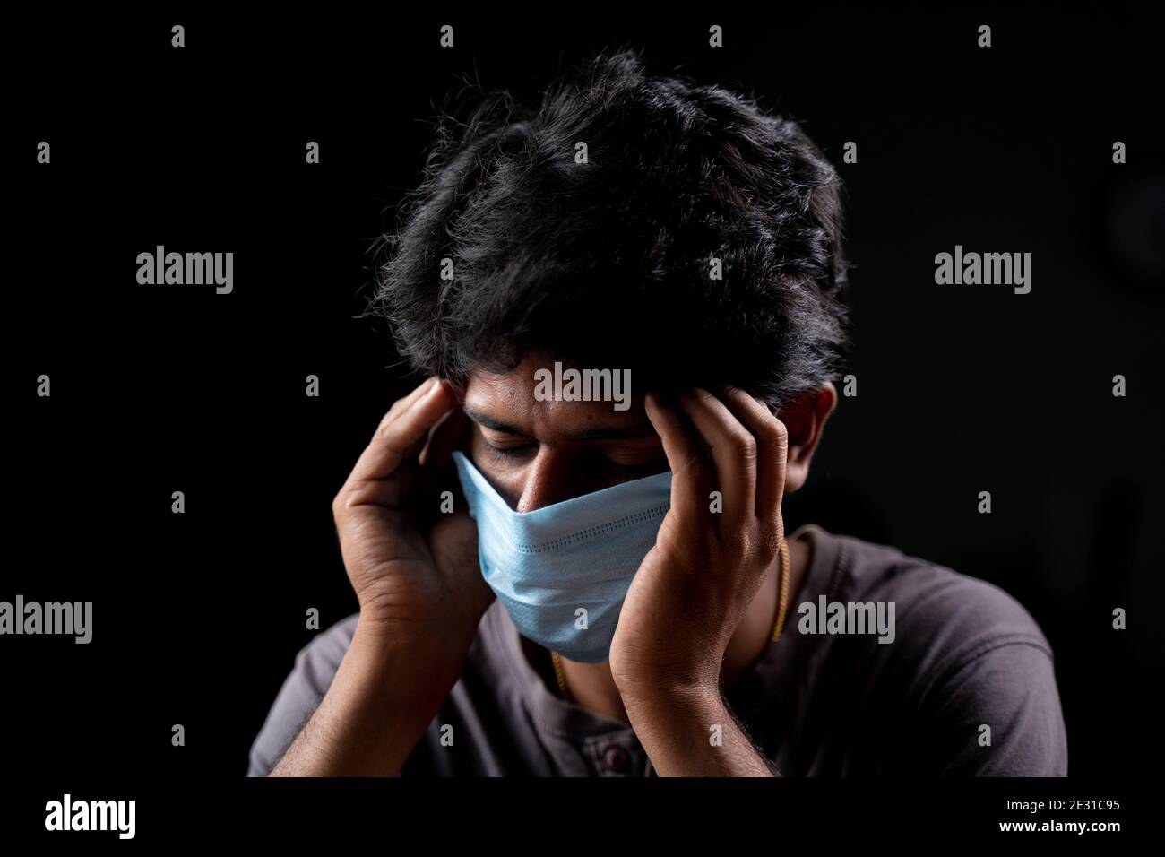Junger Mann mit medizinischer Maske hält seinen Kopf wegen Kopfschmerzen nach Impfungen - Konzept des Coronavirus covid-19 Impfung Nebenwirkungen Stockfoto