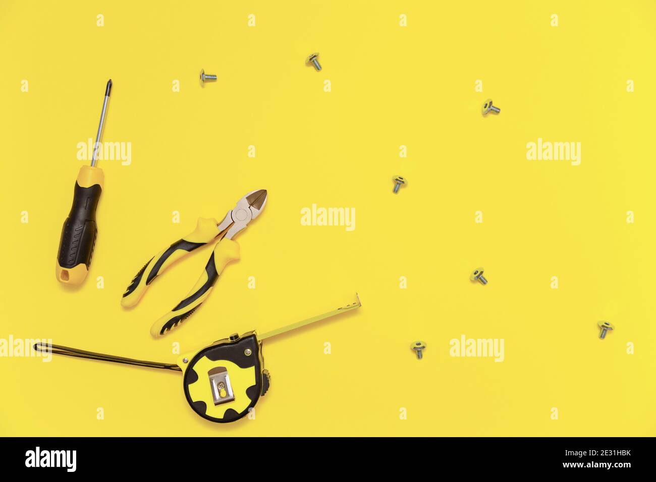Eine Flachlage mit einem Satz von Tischwerkzeugen, Schraubendreher, Schneidzange, Maßband und Schrauben auf gelb leuchtenden Hintergrund. Farben des Jahres 2021. Stockfoto
