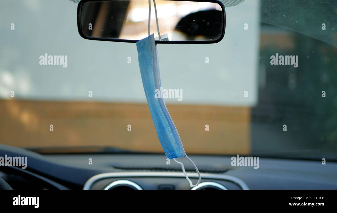 Medizinische Gesichtsmaske, die vom Fahrer verwendet wird, der auf dem aufgehängt wird Rückspiegel im Fahrzeug Stockfoto