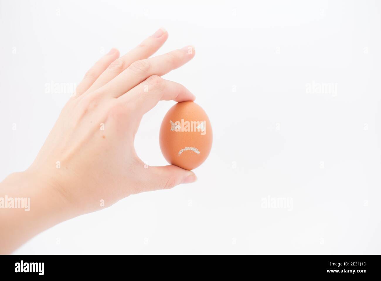 Ei mit einem frustrierten Gesicht isoliert auf weiß.Hand mit Ei Stockfoto