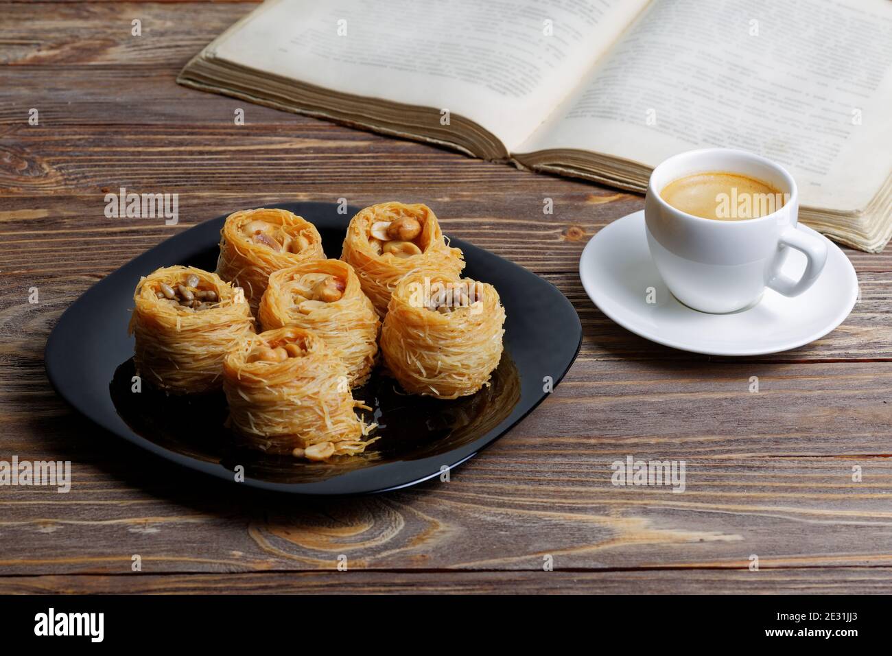 Tasse Kaffee Espresso und östlichen Süßigkeiten auf Holztisch. Buch auf verschwommenem Hintergrund öffnen. Stockfoto