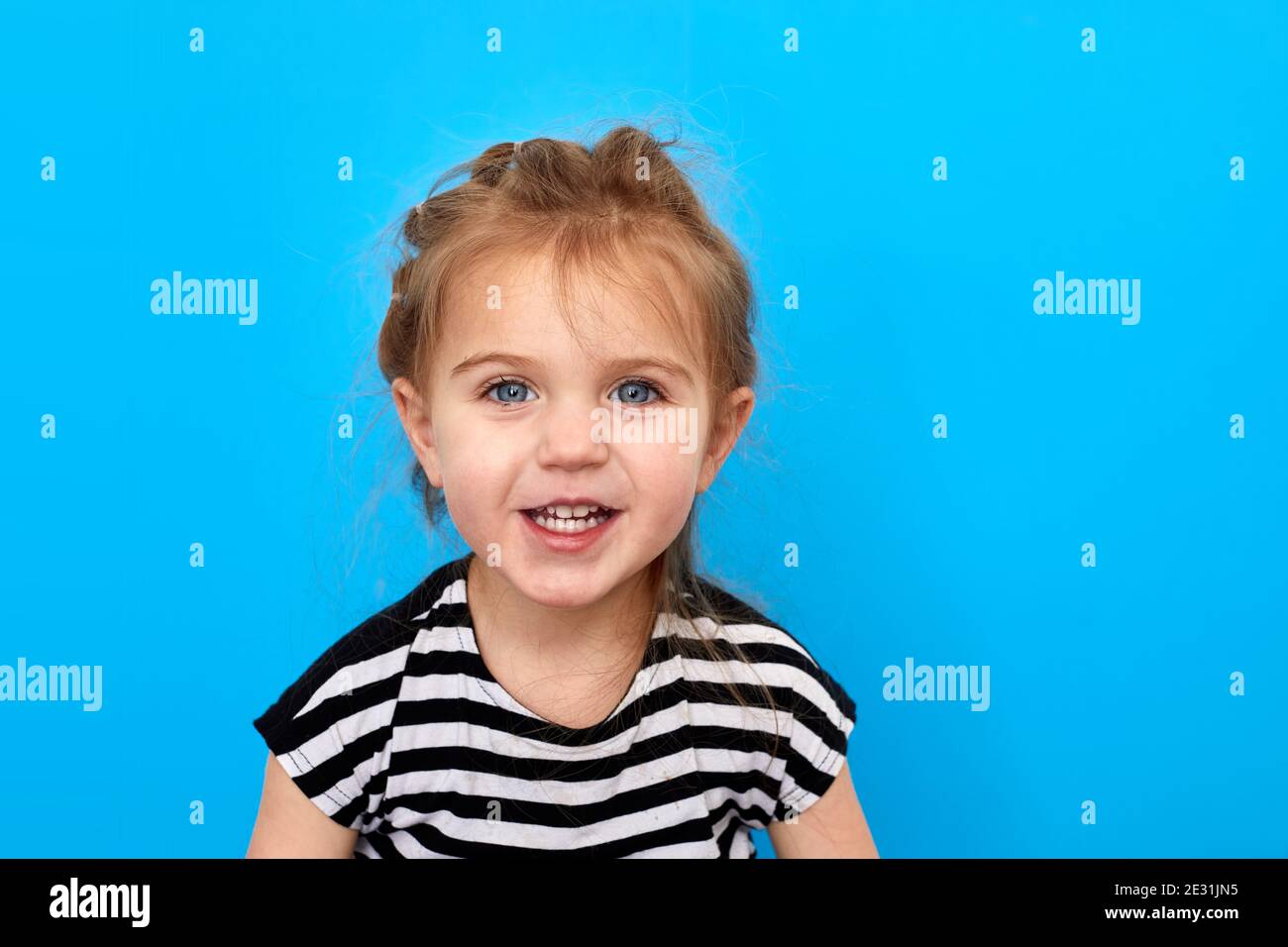 Nahaufnahme eines kleinen Mädchens im T-Shirt, das vor blauem Hintergrund posiert. Schaut auf die Kamera und lächelt Stockfoto