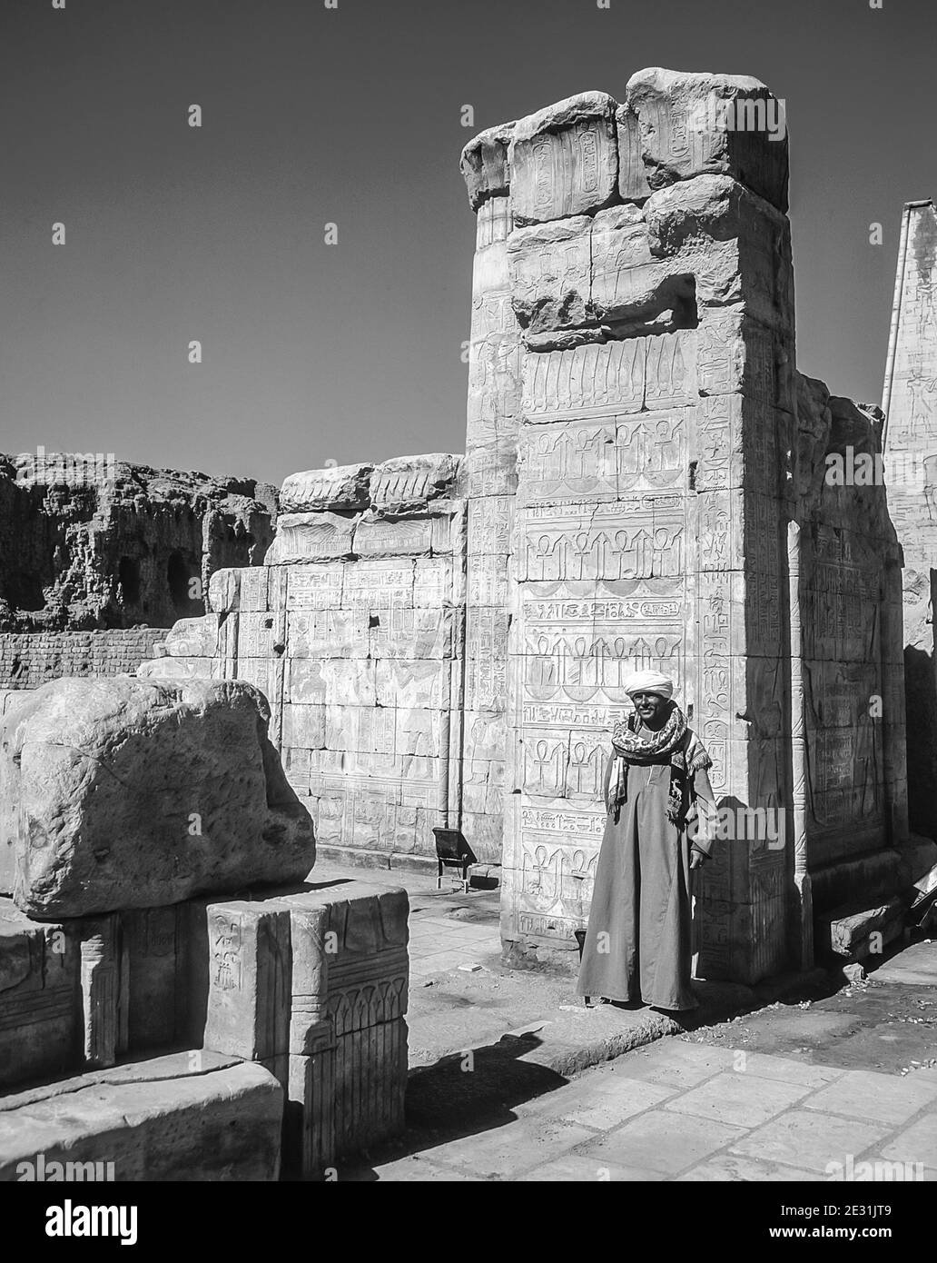 Edfu. Ein einheimischer Mann in traditioneller arabischer Kleidung bemüht sich, als inoffizieller Reiseleiter etwas Geld zu verdienen oder einfach nur für Touristen Fotos im Tempel von Horus dem Falken Gott vor 200 v. Chr. zu posieren, Auf halbem Weg zwischen Luxor und Assuan am Nil und der Stadt Edfu gelegen, die für ihre riesigen Pylonen, fein dekorierten Säulen, kartuschierten Hieroglyphen, die Wandtafeln erzählen, und feine Kunstwerke an den Decken berühmt ist. Der Tempel war glücklich, dass die Mehrheit von ihm vom Wind geblasen Sand bedeckt wurde, wodurch der Tempel von den Elementen für Jahrhunderte bewahrt wurde. Stockfoto