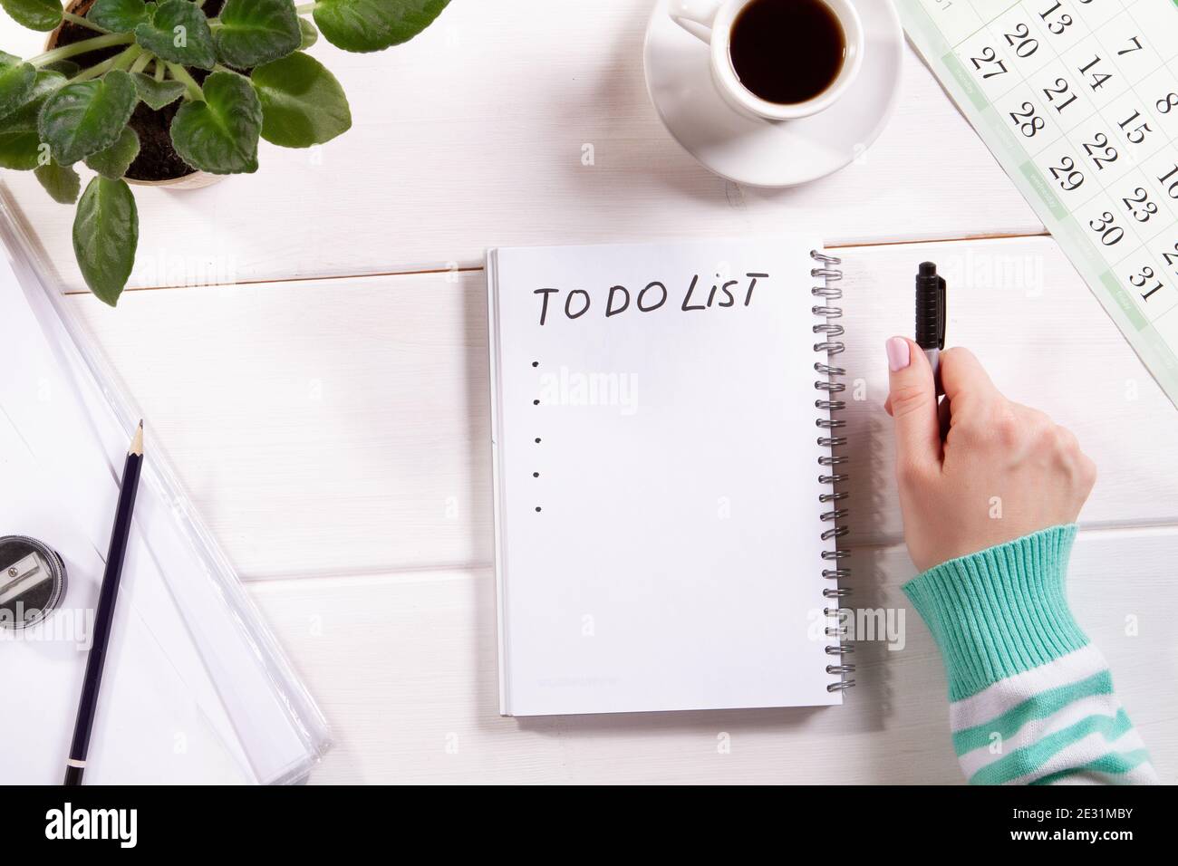 Draufsicht Mockup der Frauenhand mit Notizblock auf weißem Holz Hintergrund Kalender, Tasse Kaffee und Blume. Planung, To-Do-Liste oder Shopping. Entspannen Sie sich, w Stockfoto