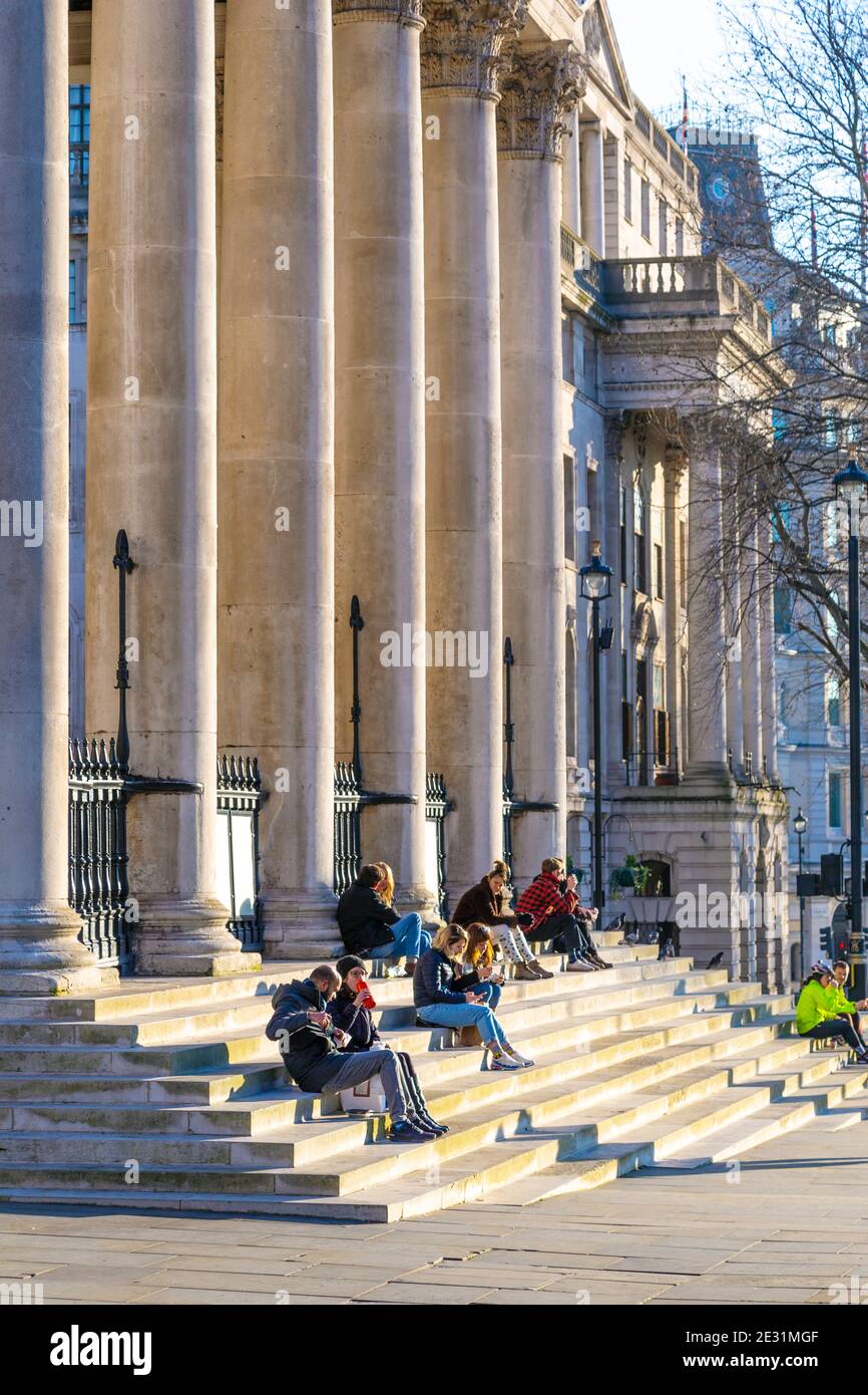 9. Januar 2021 London, UK - Menschen sitzen auf den Stufen von St. Martin-in-the-Fields auf dem Trafalgar Square während einer sonnigen Coronavirus-Epidemie sperren wir Stockfoto