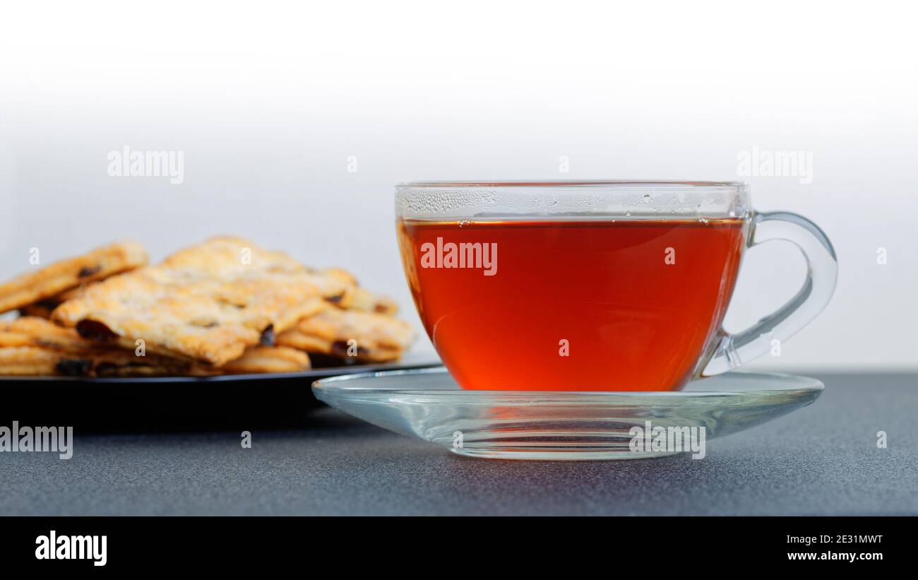 Tasse Tee auf dem dunklen Tisch gegen Blätterteig auf verschwommenem Hintergrund. Selektiver Fokus. Vorderansicht. Stockfoto