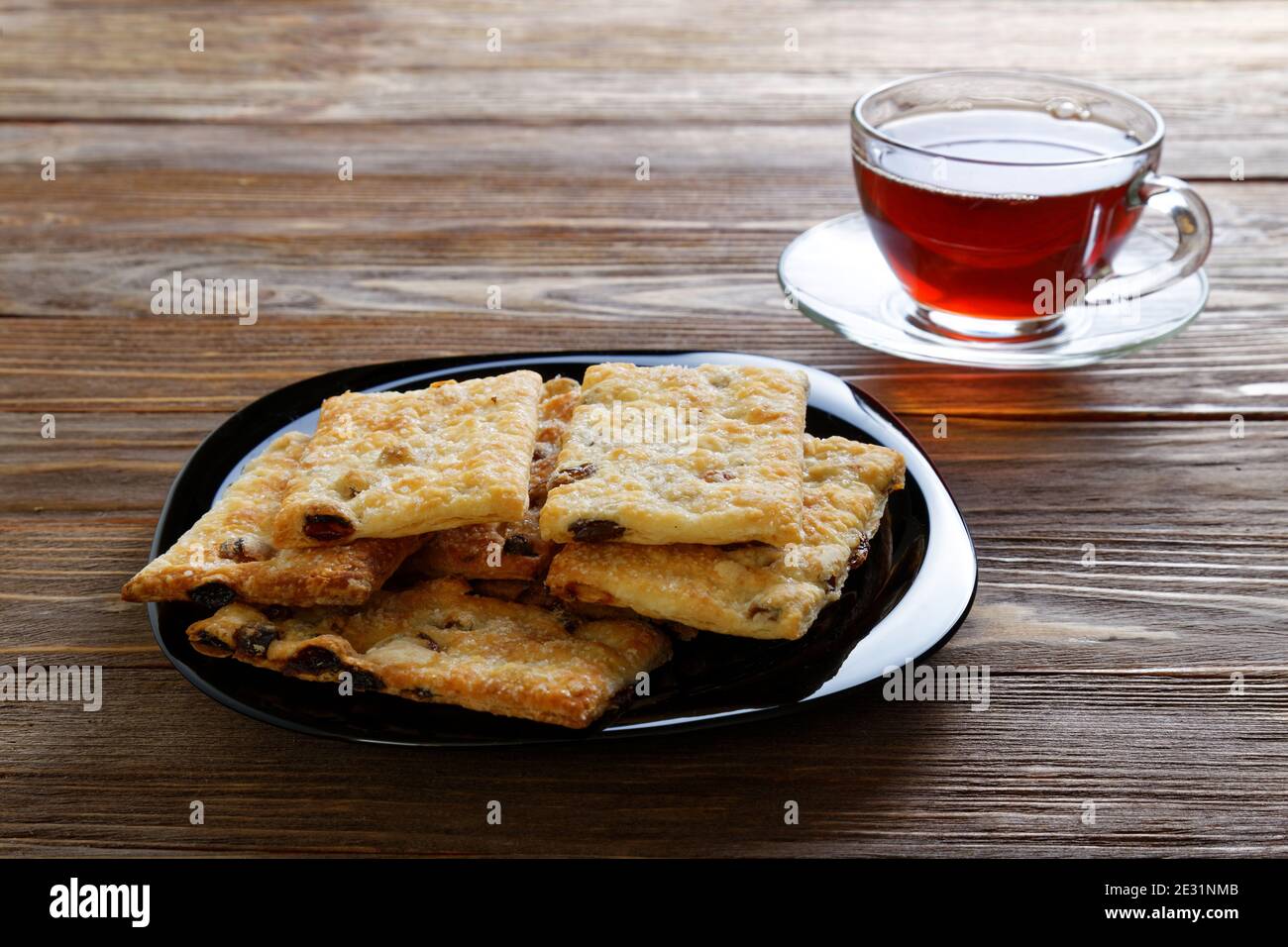 Blätterteig mit Rosinen und einer Tasse Tee im Dunkeln Brauner Holztisch Stockfoto
