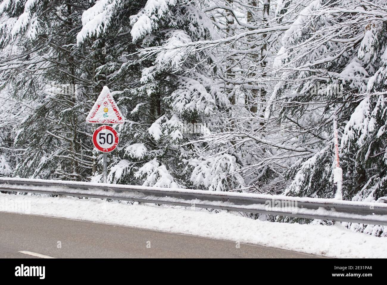 Rutschige Straße mit schneebedeckten Verkehrsschildern im Winter, Geschwindigkeitsbegrenzung 50 und Warnampel Stockfoto