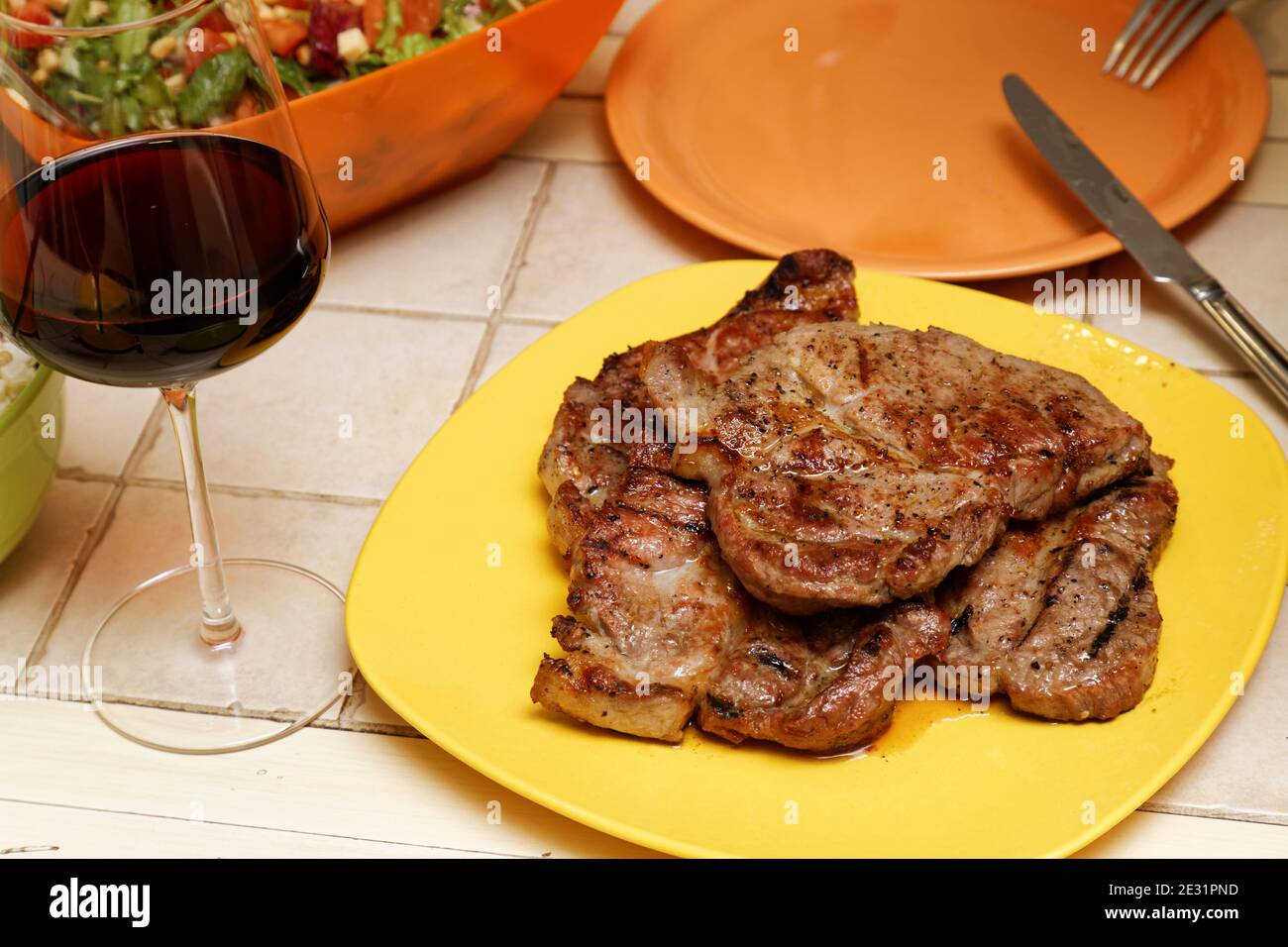 Gericht von gegrilltem Fleisch auf einem Tisch in der Nähe von einem Ein Glas Rotwein Stockfoto