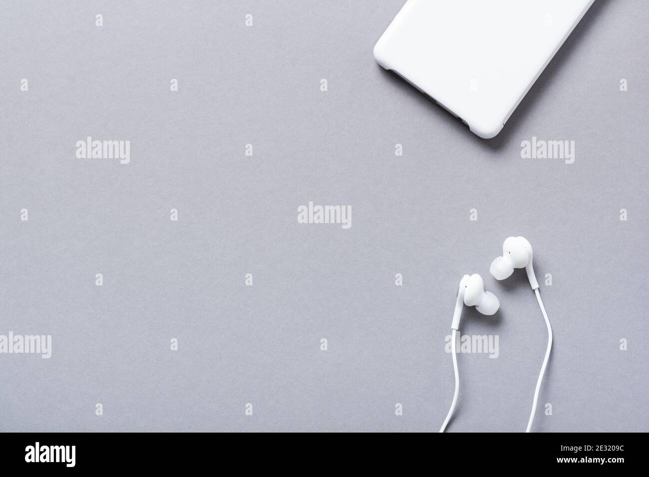 Moderne weiße Kopfhörer und Mobiltelefon auf grauem Hintergrund. Minimalistischer Stil. Draufsicht mit Kopierbereich. Stockfoto