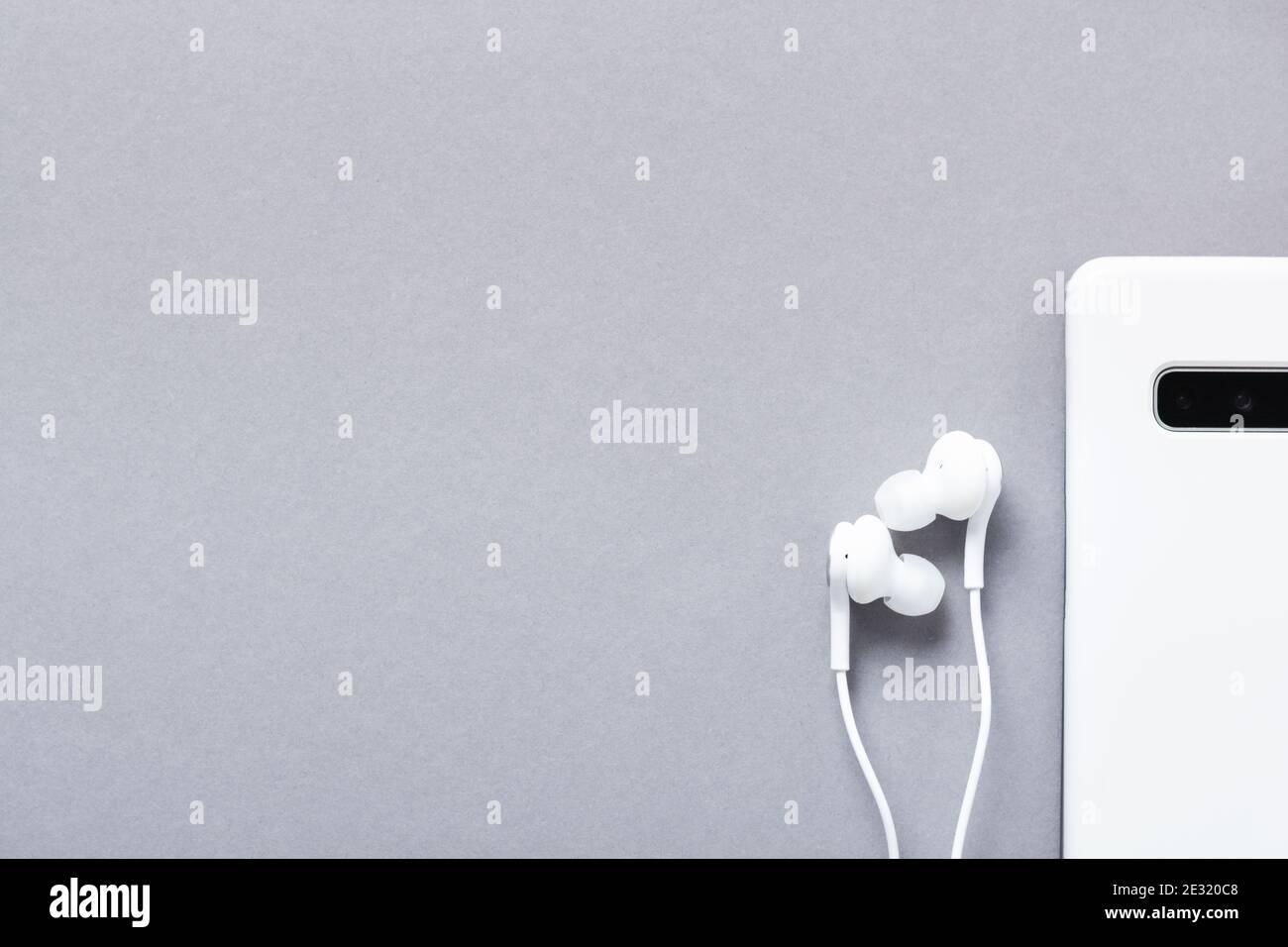 Moderne weiße Kopfhörer und Mobiltelefon auf grauem Hintergrund. Minimalistischer Stil. Draufsicht mit Kopierbereich. Stockfoto