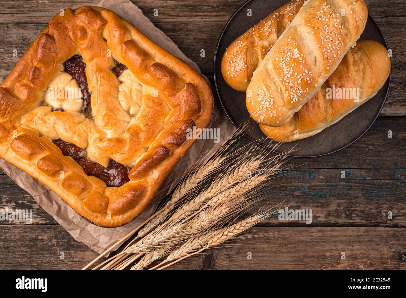 Apfelkuchen, frische Brötchen und Weizenspieß auf braunem Holzhintergrund. Stockfoto