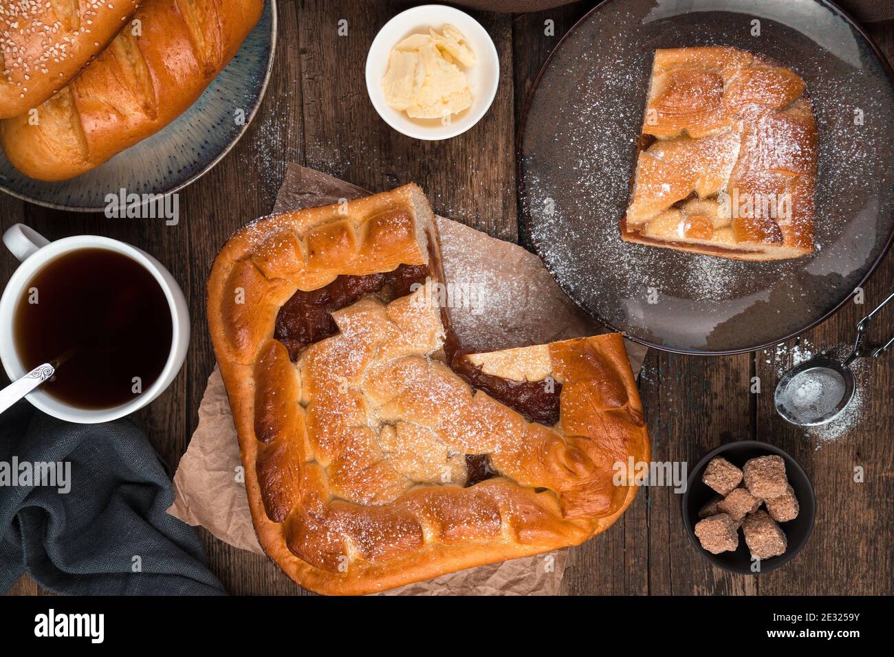 Apfelkuchen, frische Brötchen und Tee auf braunem Holzhintergrund. Stockfoto