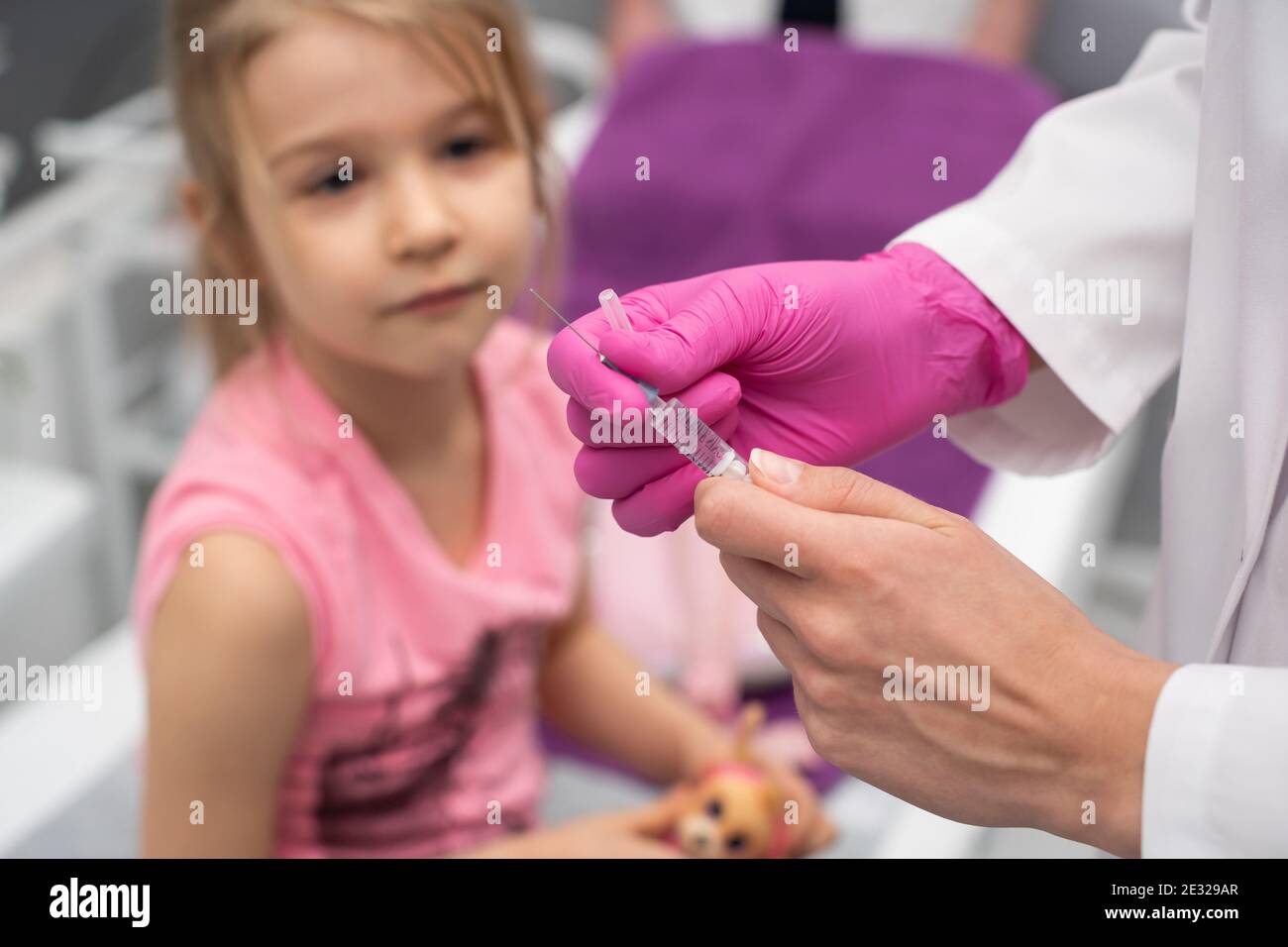 Das Kind beobachtet, wie der Arzt die Nadel und die Spritze für die Injektion vorbereitet. Eine Arztpraxis in einem öffentlichen Krankenhaus. Sichere Impfung von Kindern. Stockfoto