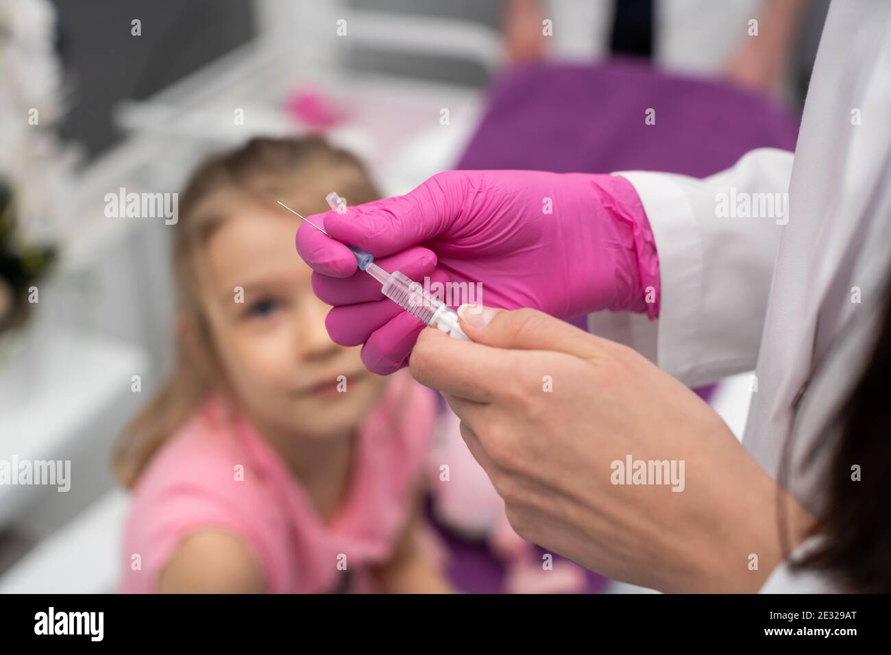 Das Kind beobachtet, wie der Arzt die Nadel und die Spritze für die Injektion vorbereitet. Eine Arztpraxis in einem öffentlichen Krankenhaus. Sichere Impfung von Kindern. Stockfoto