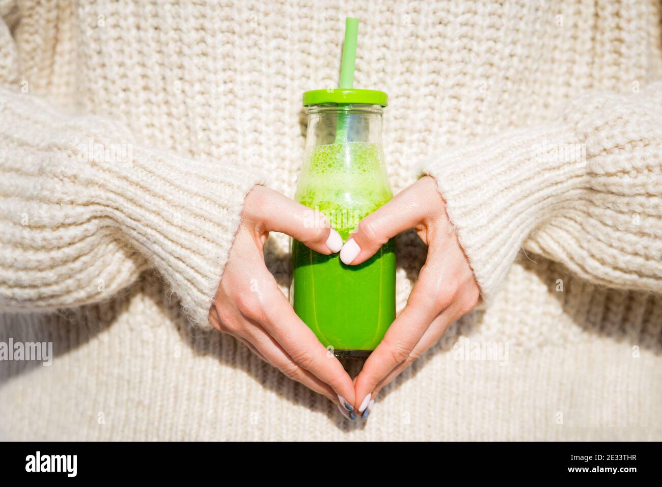 Gesundes Herz. Frau in Wollpullover Holding Flasche mit grünen hausgemachten Detox Smoothie oder Saft. Gesunder Körper, Leben, Essen, Wohnen Konzept Stockfoto
