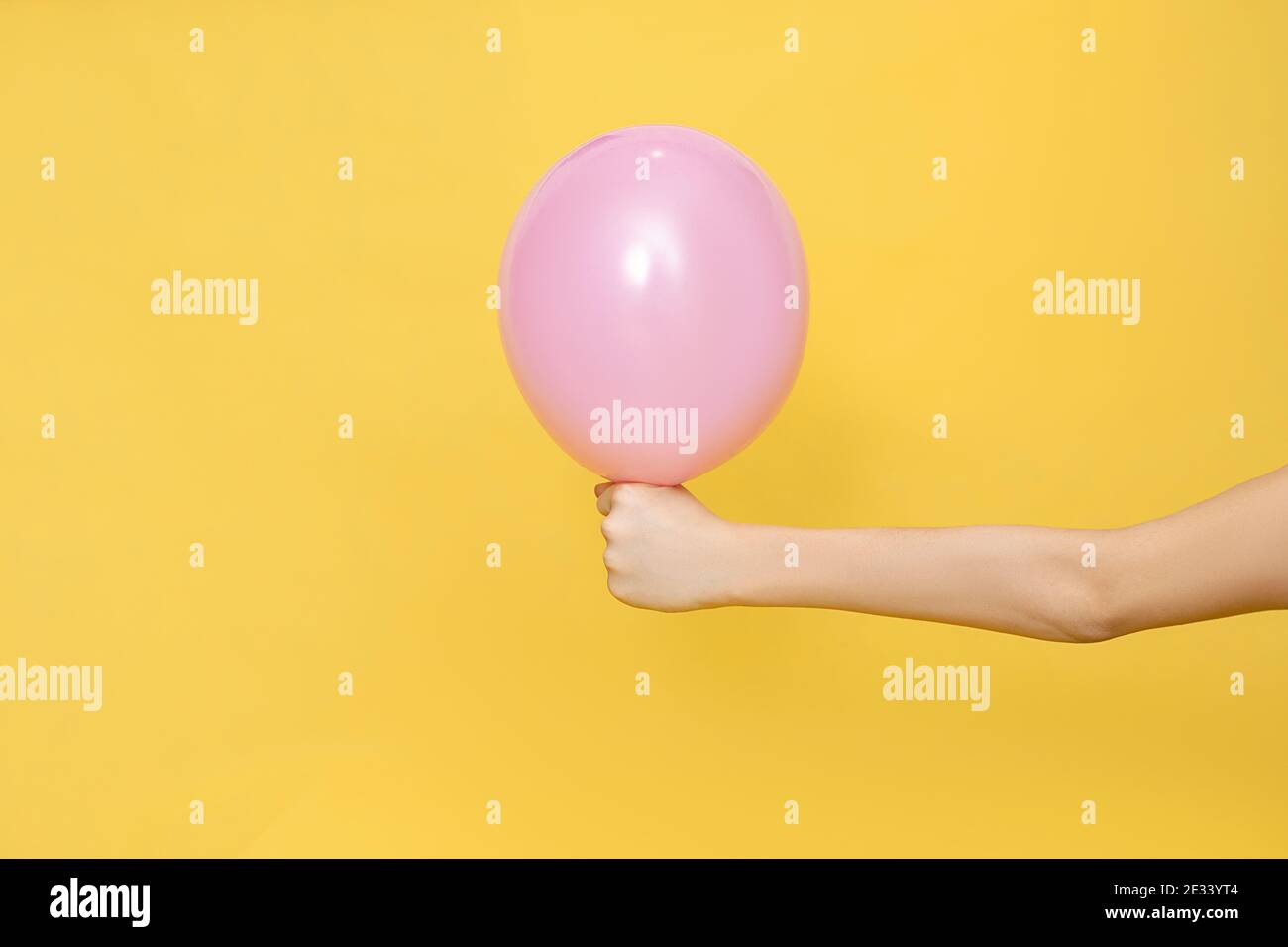 Hand halten einen rosa Ballon auf gelbem Hintergrund. Pastellfarben. Nahaufnahme Studio Foto. Konzept der Feier. Leere Stelle für Text. Stockfoto