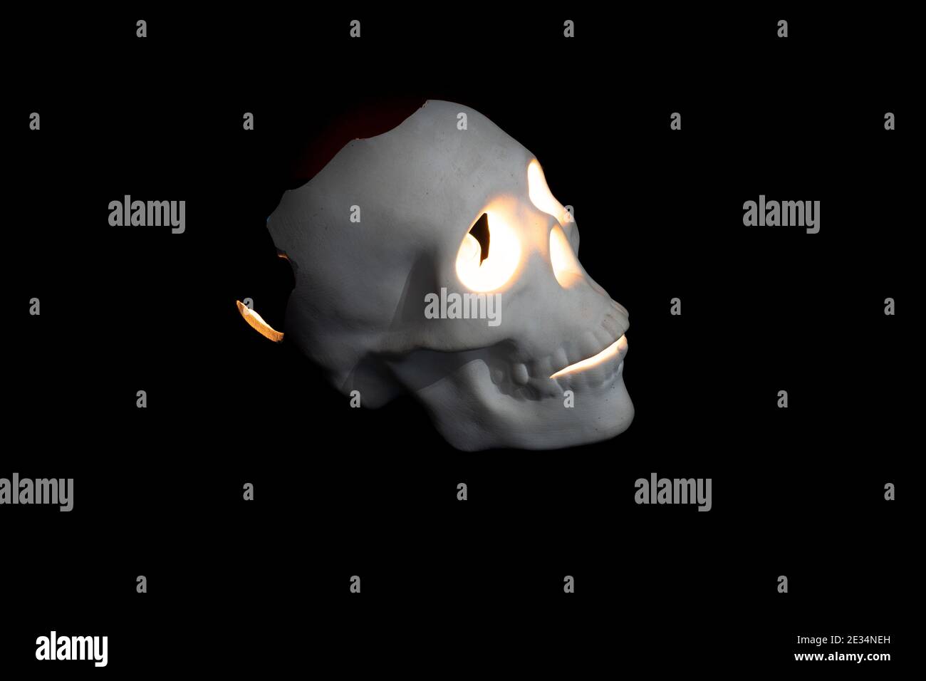 Gebrochener weißer Totenkopf auf schwarzem Hintergrund. Kerze im Inneren anzünden Stockfoto